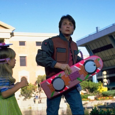 Marty McFly holding his hoverboard looking ahead with a little girl to his right.