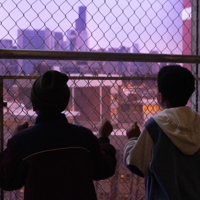 Two children looking through a mental fence at the city.