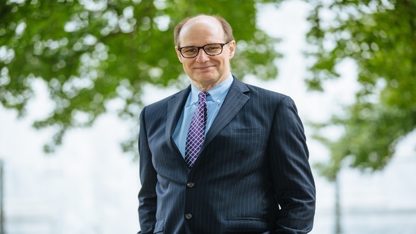 John Witte is a Caucasian man wearing dark glasses and a blue suit, pictured smiling against a backdrop of tree foliage