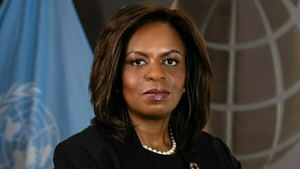 Sanda Ojiambo stands in front of a UN flag and looks at the camera