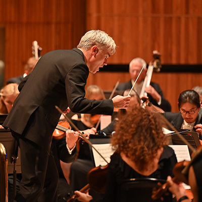 A conductor and London Philharmonic Orchestra performing.