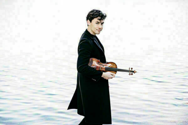 Young male violinist standing near water