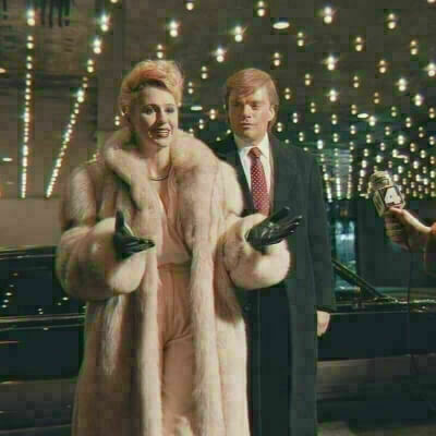 A woman in a fur coat with a man in a suit behind her