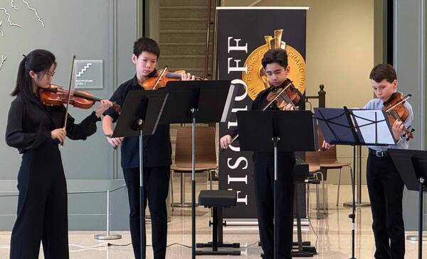 Four standing kids playing  violins in a competition